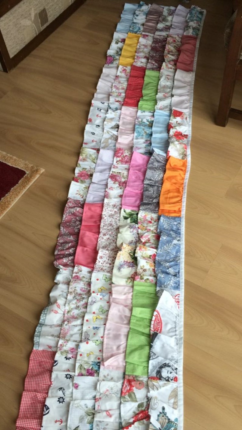 May include: A long, multi-colored fabric valance with a ruffled edge. The valance is made of various patterned fabrics, including floral prints, polka dots, and stripes. The valance is a patchwork of different fabrics, creating a unique and colorful design.