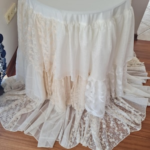 Peut inclure: Une jupe de table blanche à plusieurs couches de dentelle. La jupe est faite d'un tissu délicat et transparent et a un bord festonné. La jupe est parfaite pour ajouter une touche d'élégance à n'importe quelle table.