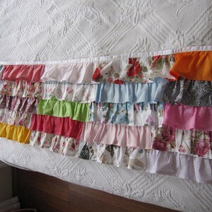 May include: A white bed with a colorful ruffled trim. The trim is made of various fabrics in different colors and patterns, including floral, plaid, and solid colors.