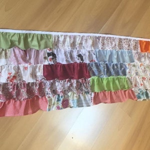 May include: A multi-colored patchwork fabric valance with ruffles. The valance is made of different fabrics with floral and geometric patterns. The valance is approximately 18 inches long and 48 inches wide.