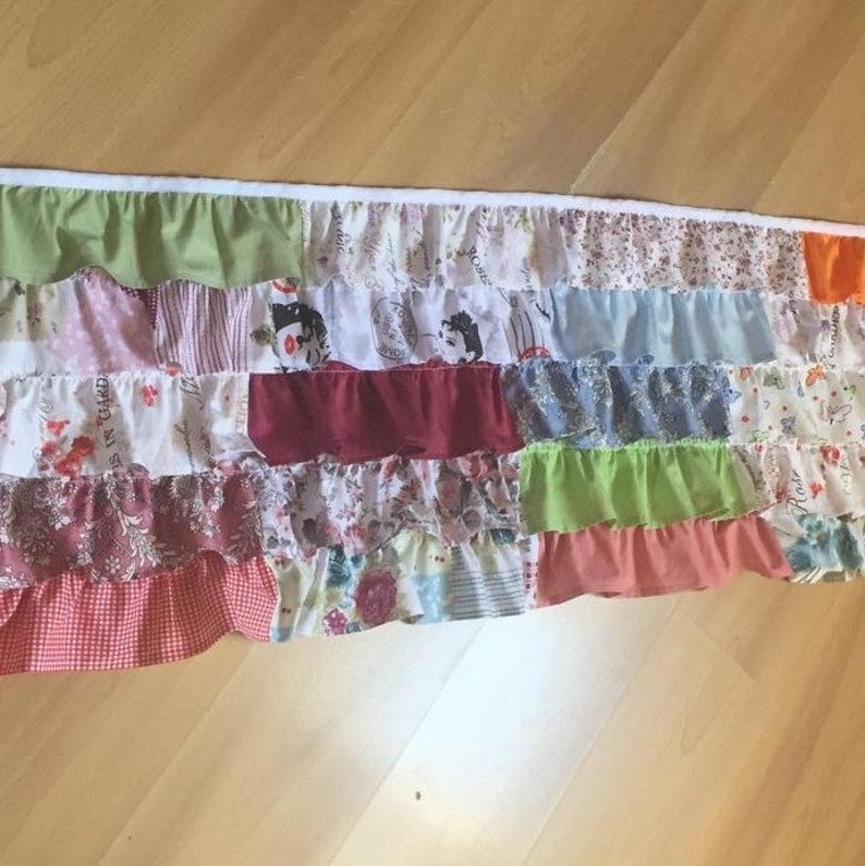 May include: A multi-colored patchwork fabric valance with ruffles. The valance is made of different fabrics with floral and geometric patterns. The valance is approximately 18 inches long and 48 inches wide.