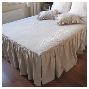 May include: A beige linen bed skirt with a ruffled edge. The skirt is on a bed with white linen pillows and a beige linen bedspread.