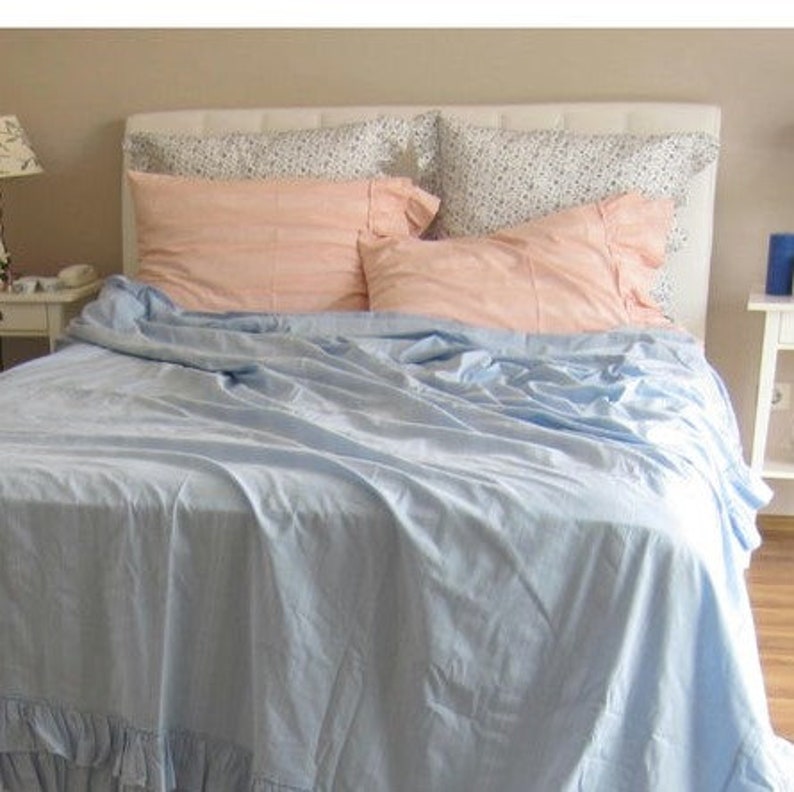 May include: A light blue bed with a white headboard and a pink and white patterned pillow. The bed is made with a light blue bedspread and has a ruffled edge.