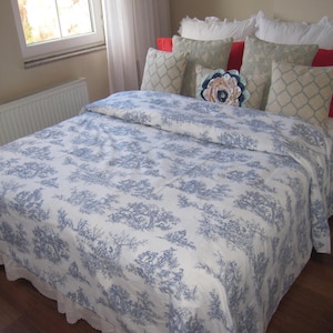 May include: A white bed with a blue and white floral patterned duvet cover. The bed is made with white pillows and a few decorative pillows with floral patterns.