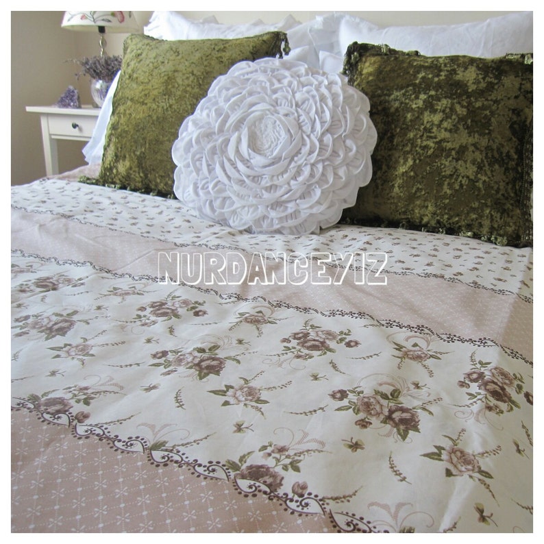 May include: A white ruffled throw pillow with green velvet pillowcases on a bed with a floral patterned bedspread.