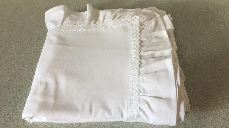 May include: White cotton bed sheet with a lace trim and ruffled edges.