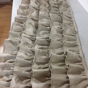 May include: A long, beige, ruffled fabric valance with multiple layers of ruffles. The fabric is a linen blend and has a slightly textured look.