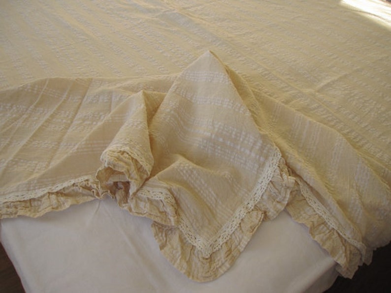 May include: A cream-colored throw blanket with a delicate lace trim. The blanket is made of a soft, textured fabric and has a subtle pattern.