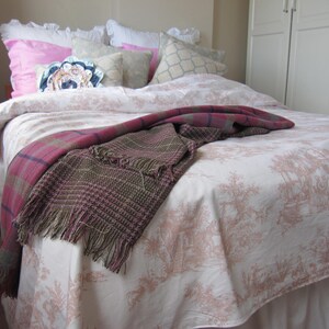 May include: A white bed with a pink and white floral patterned bedspread. The bed is made with white and pink pillows and a brown and pink throw blanket.