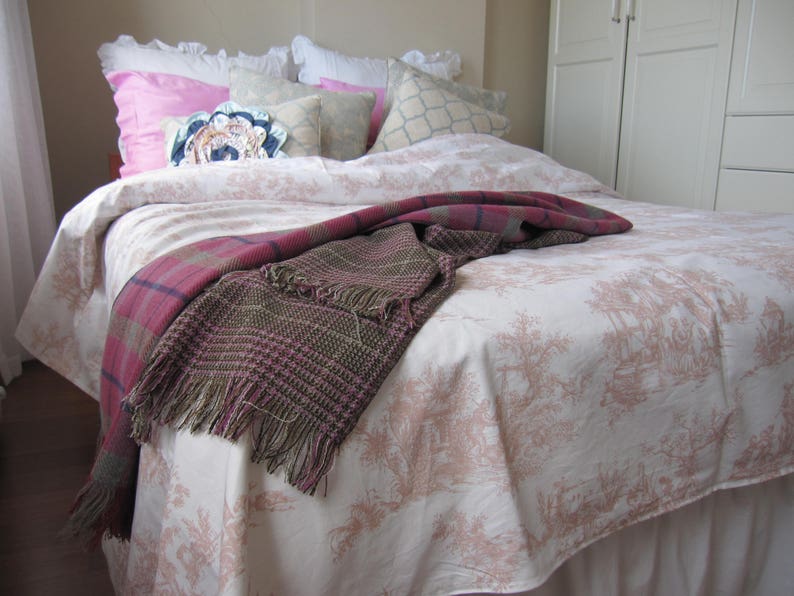 May include: A white bed with a pink and white floral patterned bedspread. The bed is made with white and pink pillows and a brown and pink throw blanket.