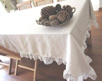 May include: A white tablecloth with a lace trim, featuring a decorative bowl filled with pine cones.