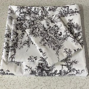 May include: White fabric with a black and white toile pattern featuring a repeating design of trees, flowers, and figures. The fabric has a soft, smooth texture.