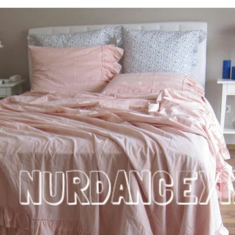 May include: A pink ruffled bedspread with a white and floral patterned pillow and a pink pillow with a ruffled edge.