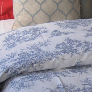 May include: A white duvet cover with a blue toile pattern featuring a repeating design of trees, houses, and figures. The duvet cover is made of a soft, lightweight fabric.