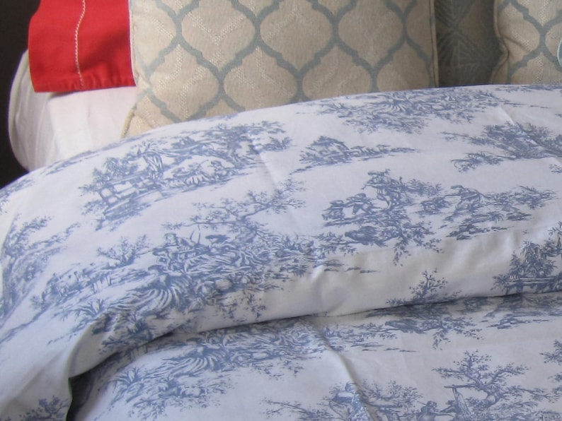 May include: A white duvet cover with a blue toile pattern featuring a repeating design of trees, houses, and figures. The duvet cover is made of a soft, lightweight fabric.
