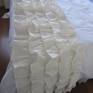 May include: A white ruffled bed skirt with a delicate, layered design. The skirt is made of soft, flowing fabric and adds a touch of elegance to any bedroom.