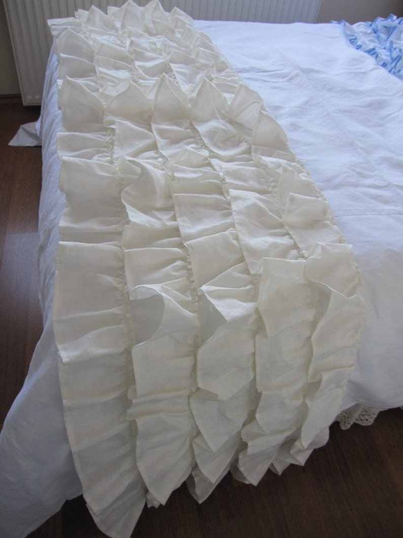 May include: A white ruffled bed skirt with a delicate, layered design. The skirt is made of soft, flowing fabric and adds a touch of elegance to any bedroom.