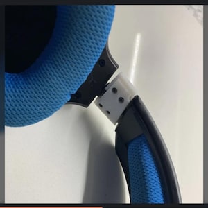 May include: A close-up of a gaming headset, featuring blue mesh earcups and a black headband. The plastic components are white and black, with visible screws. The design suggests a focus on comfort and audio quality for extended use.