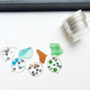 May include: A collection of sea glass, beads, and wire for making jewelry. The sea glass is in shades of blue, green, and brown. The beads are white, blue, and green. The wire is silver.