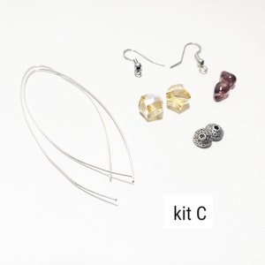 May include: A kit for making earrings with two silver earring hooks, two silver spacer beads, two clear faceted beads, and two purple heart-shaped beads. The kit is labeled "kit C".