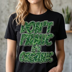 Może przedstawiać: Czarny t-shirt z napisem "DON'T PANIC IT'S ORGANIC" w kolorze zielonym, z wzorem liści. Koszulka ma okrągły dekolt i wydaje się być wykonana z bawełny. Projekt jest wyśrodkowany z przodu.