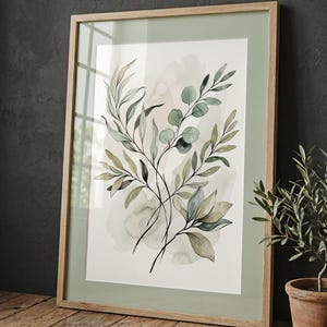 May include: A framed wall art print featuring a watercolor illustration of botanical branches with green and sage leaves. The artwork is set against a soft cream background with muted green watercolor washes, enclosed in a light wood frame.