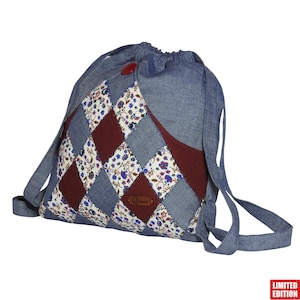 Könnte beinhalten: Ein Jeans-Rucksack mit Kordelzug und Patchwork-Design. Der Patchwork-Stil zeigt ein Rautenmuster aus floralem Stoff, Jeansstoff und bordeauxfarbenem Stoff. Ein roter Knopf sichert die obere Klappe. Die Tasche hat Jeansriemen.
