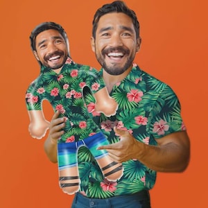 May include: A man wearing a tropical print shirt with green leaves and pink flowers, holding a cutout of himself wearing the same shirt. The cutout has blue and green striped shorts and black and white striped socks. The background is orange.