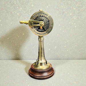 Può includere: Replica di telegrafo navale in ottone con base in legno. Il quadrante circolare indica "Ship Telegraph" e presenta indicatori direzionali come "Stop", "Slow" e "Full". La base è marrone scuro e il design è vintage.