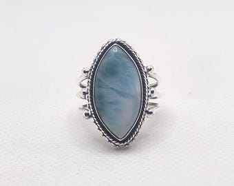 May include: A silver ring with an oval, pale blue gemstone. The stone is set in a detailed silver frame with a braided edge and decorative accents. The ring has a vintage or artisan style, suitable for everyday wear.