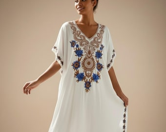 May include: White caftan dress with a V-neck and short sleeves. The dress features intricate embroidery in brown and blue floral patterns around the neckline and sleeves. The dress is floor-length and has a relaxed fit.