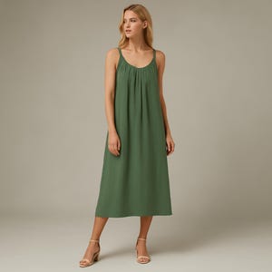May include: A green midi dress with spaghetti straps and a gathered bodice. The dress has a flowing, A-line skirt and is made of a lightweight fabric. The model is wearing nude-coloured heels.