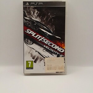 May include: A PSP video game case for Split/Second Velocity featuring a black and white graphic of a sports car in motion. The cover includes the PSP logo at the top, a PEGI 7 age rating in the bottom left corner, and a white price sticker on the front.