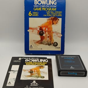 Op de afbeelding: Een vintage Atari Bowling videogame set. De blauwe doos toont de speltitel en afbeeldingen van een bowler. Inclusief een spelcartridge en instructiehandleidingen. De spelcartridge is zwart met het woord "bowling".