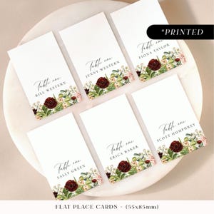 Tarjetas de lugar para bodas de otoño en color burdeos, tarjetas con nombres de invitados impresos con flores otoñales, tarjetas de lugar planas o plegadas con motivos florales y helechos.