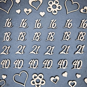 Peut inclure: Découpes en bois avec les chiffres 16, 18, 21 et 40, ainsi que des formes de cœur et de fleur. Les chiffres sont écrits en cursive. Les découpes sont disposées sur une surface gris foncé, pour le bricolage ou les décorations d'événements.