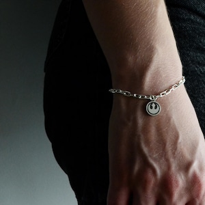 Op de afbeelding: Zilveren kettingarmband met een ronde bedel met een zwart-witte afbeelding. De armband wordt om de pols gedragen, met een donkere achtergrond.