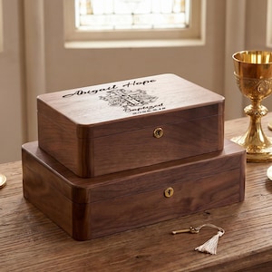 May include: Two stacked wooden boxes, one with a key and tassel. The top box is engraved with the name "Abigail Hope" and the word "Baptized". Gold candlesticks, a chalice, and a plate with wafers are also present.