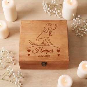 May include: A square wooden box with a hinged lid featuring a laser-engraved illustration of a sitting dog wearing a collar with a bow. Below the dog, the name Harper is engraved in script, followed by the years 2012-2026 and four small hearts.
