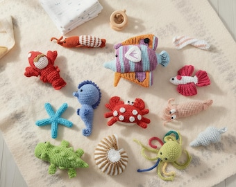 May include: A collection of colorful, crocheted sea creatures and toys, including a starfish, seahorse, crab, fish, and octopus. The toys are arranged on a cream-colored blanket, alongside a folded white cloth and a wooden ring.