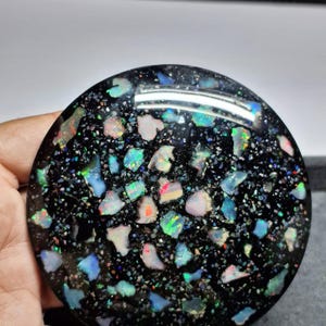 May include: A round, polished black opal stone with a mosaic of colorful opal fragments. The fragments display a range of colors including blue, green, pink, and orange, creating a vibrant, speckled appearance. The stone has a glossy finish.