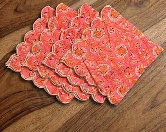 Pode incluir: Seis bases para copos cor-de-rosa com padrão floral e bordas onduladas. O padrão repetido apresenta flores e folhas laranja. As bordas são bordadas com uma borda creme. As bases para copos estão dispostas sobre uma superfície de madeira.