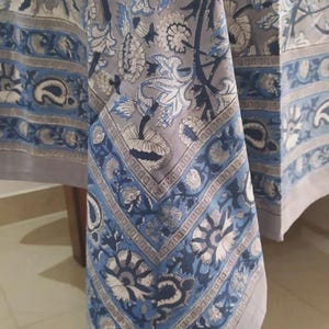 May include: A grey tablecloth featuring a detailed floral and paisley print in shades of dark blue and light blue. The fabric displays a wide decorative border with intricate botanical patterns and a central section with larger floral motifs.