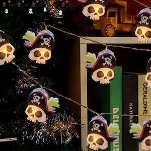May include: String of Halloween-themed lights featuring skull-shaped bulbs wearing pirate hats. The lights are strung on a thin wire, with each skull illuminated. The background includes a bookshelf and decorative elements, creating a festive atmosphere.
