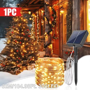 Puede incluir: Escena festiva al aire libre con un árbol de Navidad y una casa decorada con luces de cadena. Un panel solar alimenta una cadena de 32 metros (104.98 pies) de 300 LED, ideal para la decoración navideña.