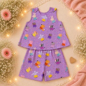 May include: A purple sleeveless top and matching shorts set featuring an all-over print of various cartoon animals including pigs, rabbits, and zebras. The top has two purple buttons at the shoulders and a flared silhouette with a colourful confetti pattern.
