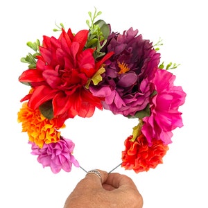 Op de afbeelding: Een levendige bloemenkrans met een verscheidenheid aan kleurrijke bloemen. De krans bevat rode dahlia's, paarse pioenrozen en roze, oranje en paarse bloemen, geaccentueerd met groen blad. De bloemen zijn gerangschikt op een draadbasis.