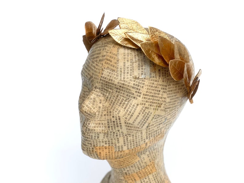 May include: A gold leaf crown headband with a simple design. The headband is made of leaves that are attached to a wire base.
