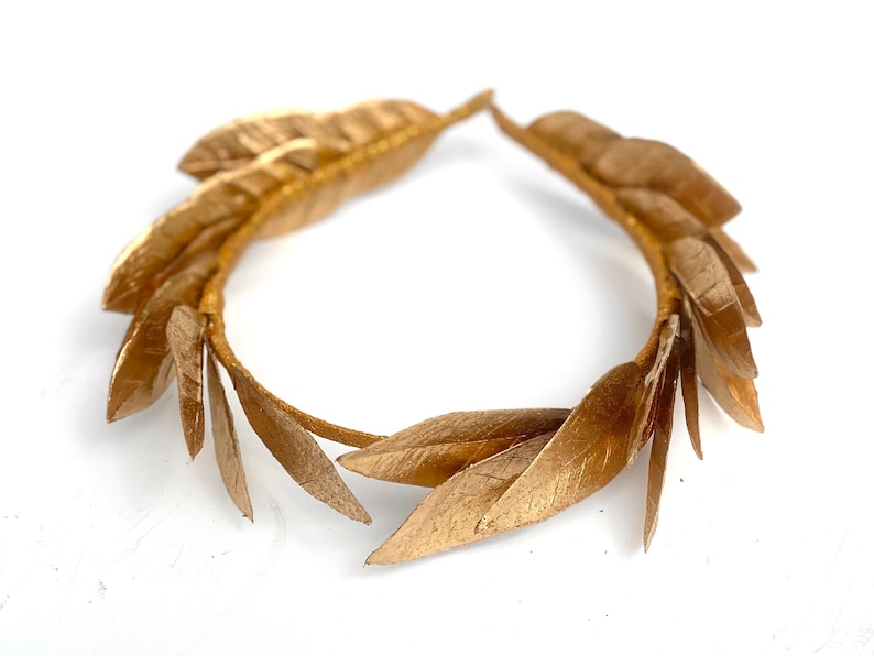May include: A gold laurel wreath headband with a circular shape and multiple leaves.
