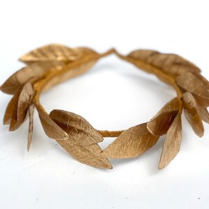 May include: A gold laurel wreath made of metal leaves. The wreath is a circle and is made of many individual leaves.